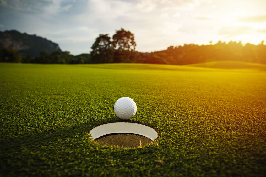 A golf ball on the brink of falling in the cup on the green